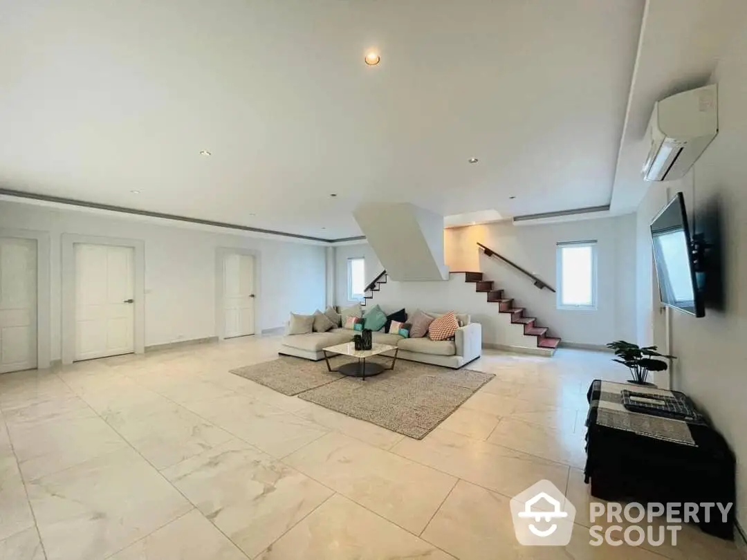 Spacious living room with elegant marble flooring, modern furniture, and a stylish staircase leading to the upper level, perfect for luxurious living.