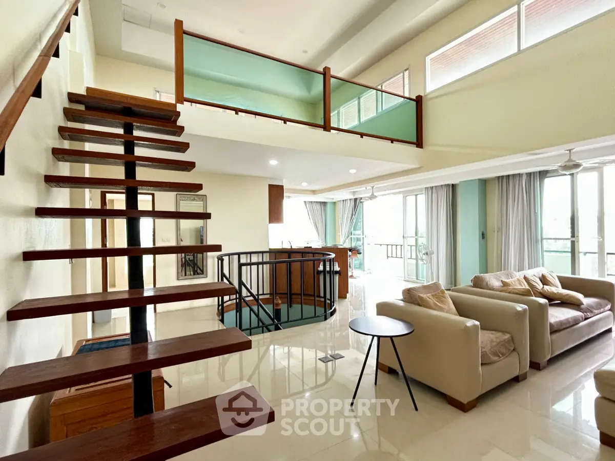 Spacious modern living room with open staircase and large windows offering natural light.