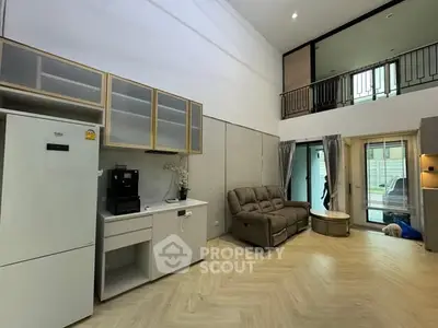 Spacious modern living room with high ceiling and mezzanine, featuring cozy sofa and sleek kitchen area.