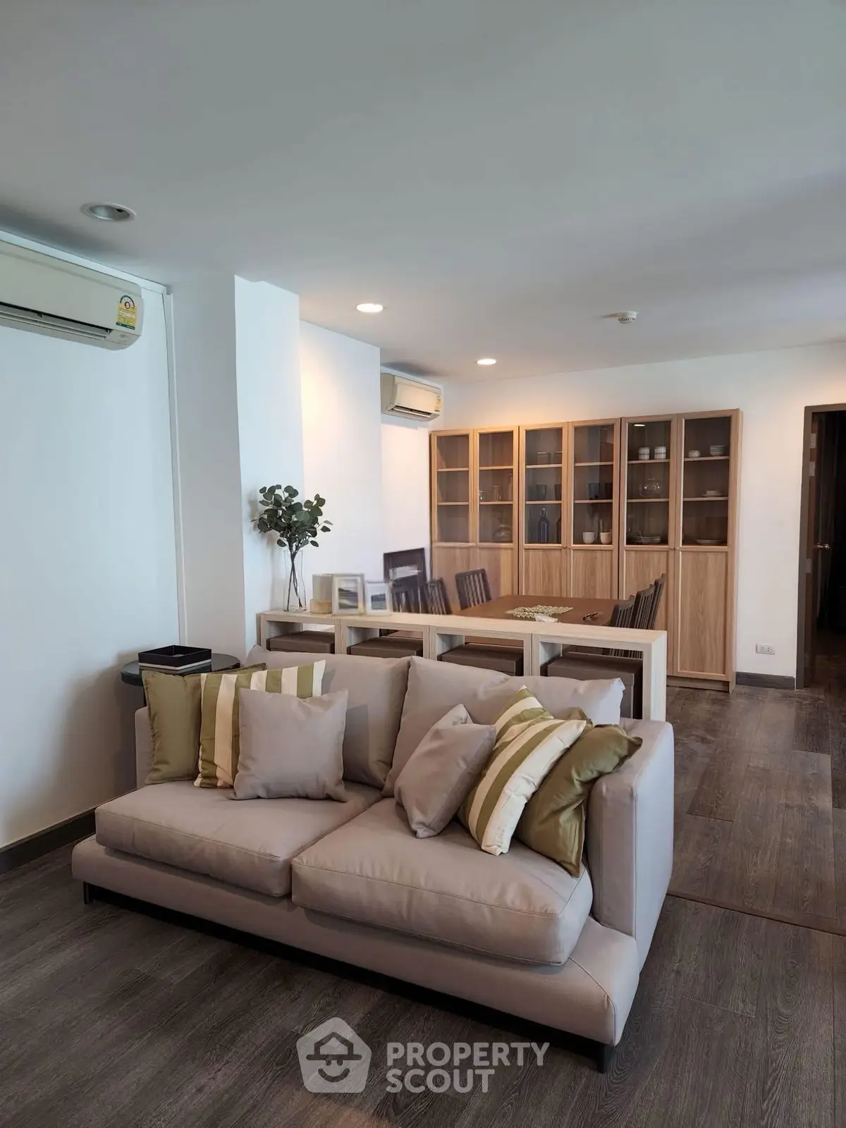Spacious living room with modern decor and dining area, featuring elegant wooden flooring and stylish furniture.