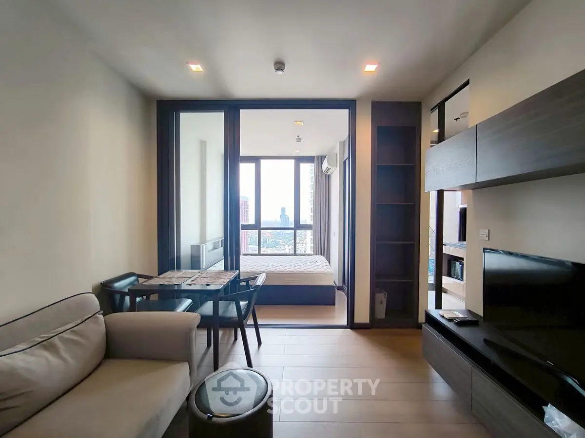 Modern apartment with open living room and bedroom, featuring city view and sleek furnishings.