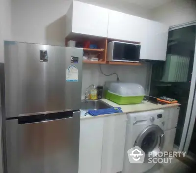 Modern kitchen with stainless steel fridge, washing machine, and microwave in compact layout.