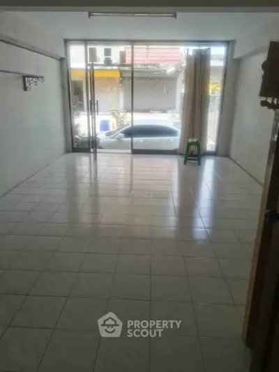 Spacious tiled room with large glass doors and street view, ideal for versatile use.