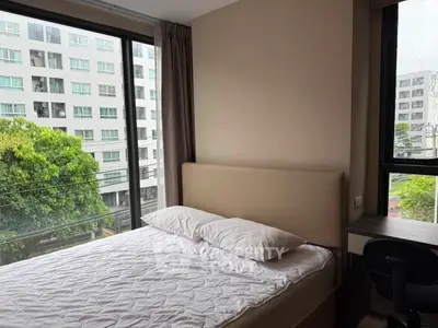 Modern bedroom with large windows offering a city view, featuring a comfortable bed and a study desk.