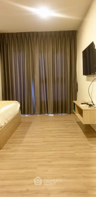 Modern bedroom with wooden flooring, wall-mounted TV, and elegant curtains.