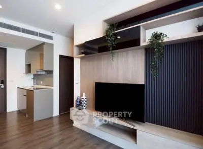 Modern living room with sleek TV unit and open kitchen layout, featuring stylish decor and wooden flooring.