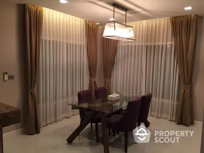 Elegant dining area with glass table and purple chairs, featuring floor-to-ceiling curtains.