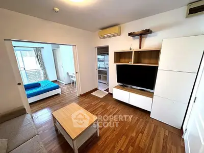 Modern living room with wooden flooring, open layout, and view into bedroom