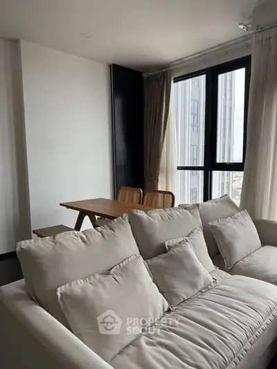 Modern living room with cozy sofa and dining area, featuring large windows and natural light.