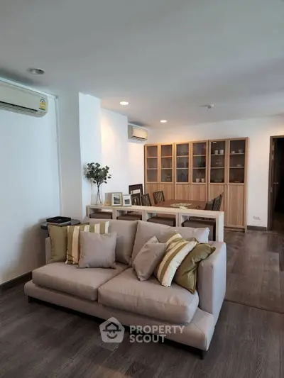 Spacious living room with modern decor and dining area, featuring elegant wooden flooring and stylish furniture.