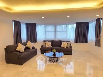 Spacious living room with elegant sofas and large windows, featuring a modern ceiling design and marble flooring.