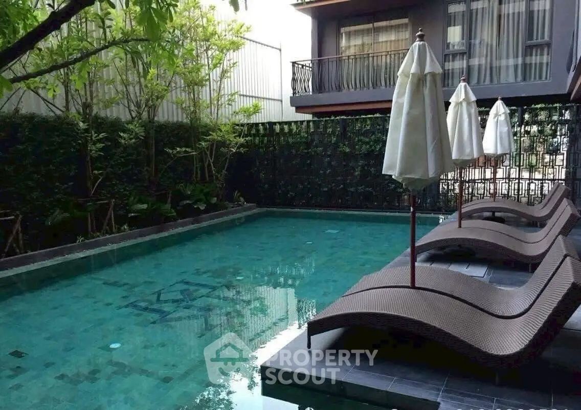 Luxurious residential pool area with stylish loungers and umbrellas, surrounded by lush greenery.