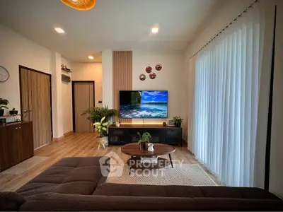 Modern living room with stylish decor and large TV, featuring cozy seating and natural light.
