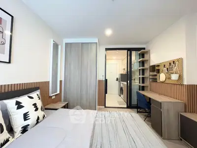 Modern bedroom with stylish decor and workspace, featuring sliding closet doors and a view into the kitchen area.