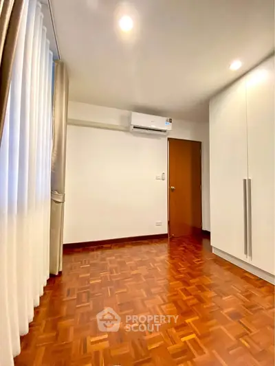 Spacious bedroom with wooden flooring and modern air conditioning unit