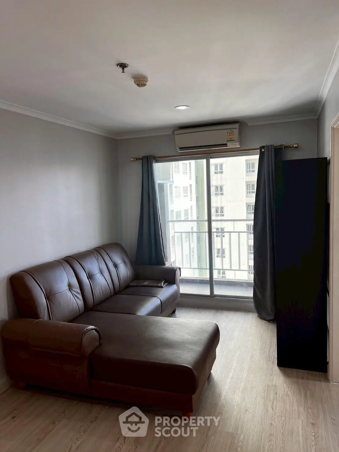Modern living room with leather sofa and balcony view in high-rise apartment.