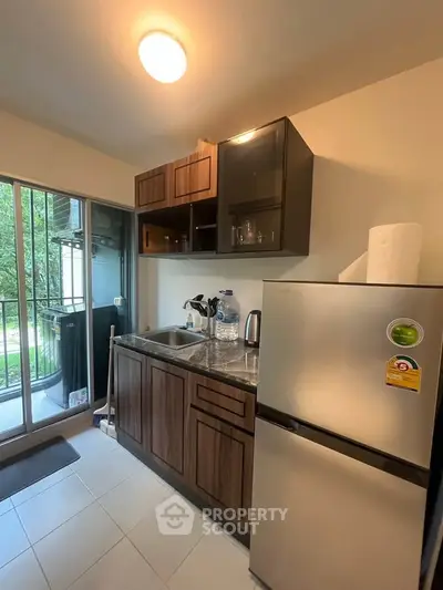 Modern kitchen with sleek cabinets and stainless steel fridge, featuring a view of the lush greenery outside.