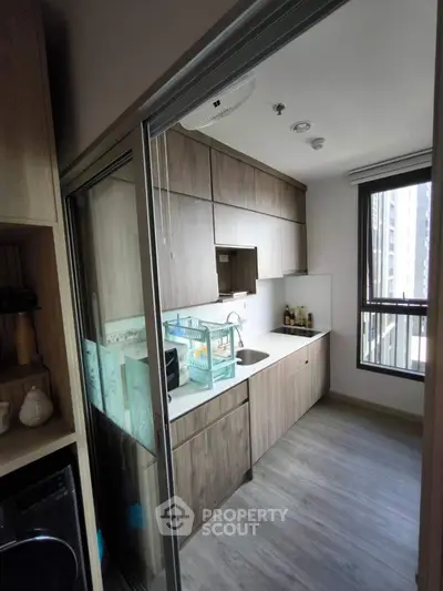 Modern kitchen with sleek cabinetry and large window in urban apartment