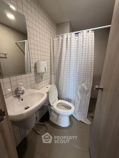Modern bathroom with tiled walls, shower curtain, and sleek fixtures in a contemporary apartment.