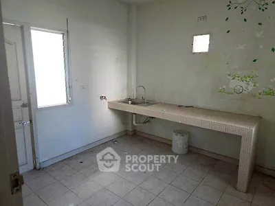 Spacious kitchen with minimalist design and ample natural light, featuring a long countertop and tiled flooring.