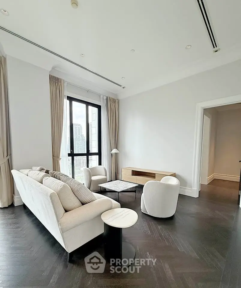 Elegant living room with modern furniture and city view, featuring dark wood flooring and large windows.