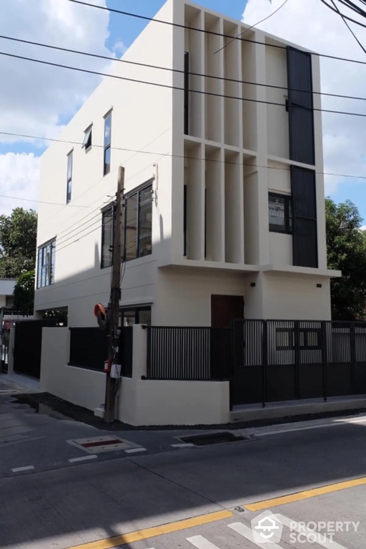 Modern three-story building with sleek facade and gated entrance on a sunny day.