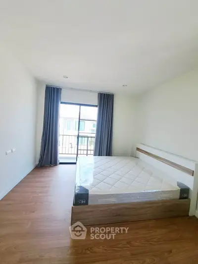 Spacious bedroom with large window and balcony access, featuring modern wooden flooring and minimalist design.