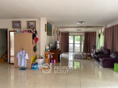 Spacious living room with glossy tiled flooring, large windows draped with curtains, and an array of personal items and furniture.