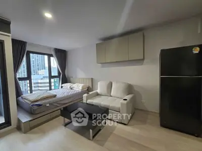 Modern studio apartment with bed, sofa, and fridge, featuring sleek design and city view.