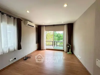 Spacious living room with large windows and balcony access, featuring modern lighting and hardwood floors.