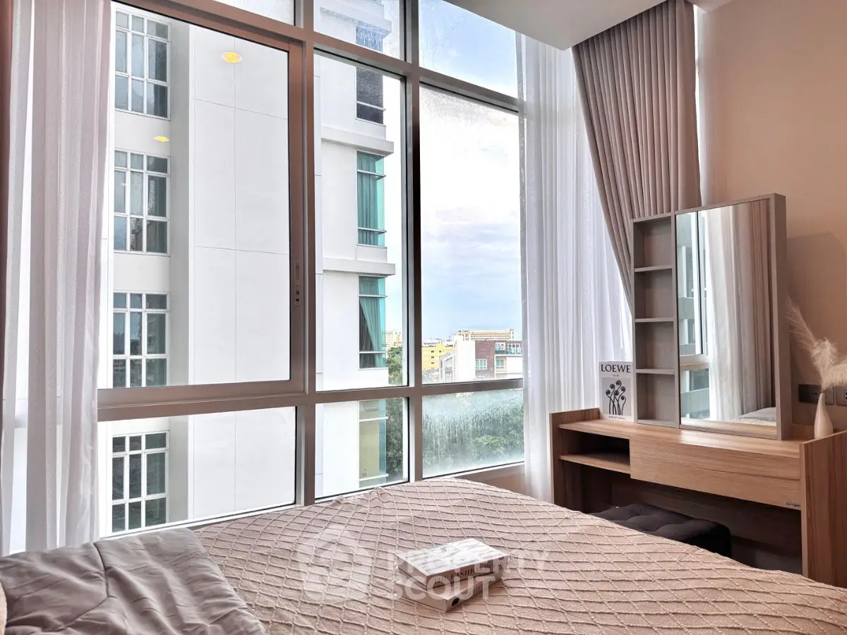 Bright bedroom with large windows offering city views and modern furnishings.