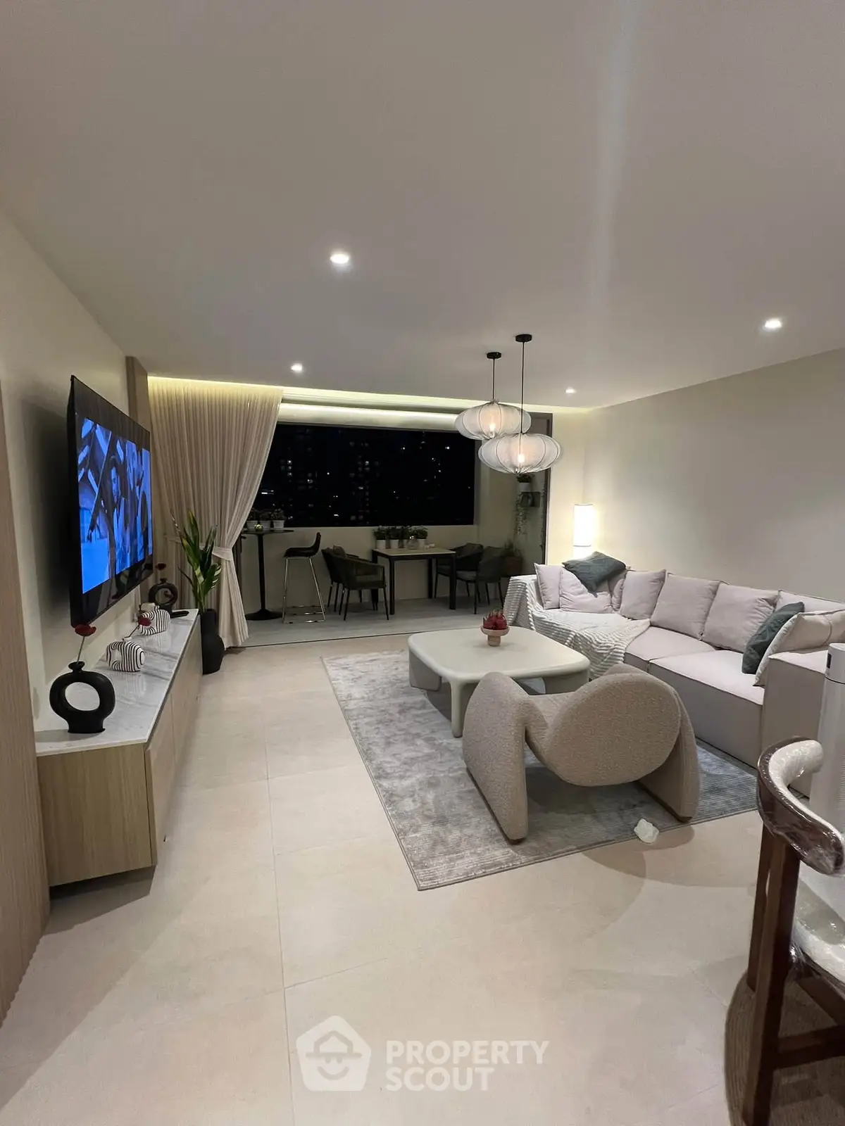 Modern living room with stylish furniture and ambient lighting, featuring a large TV and elegant decor.