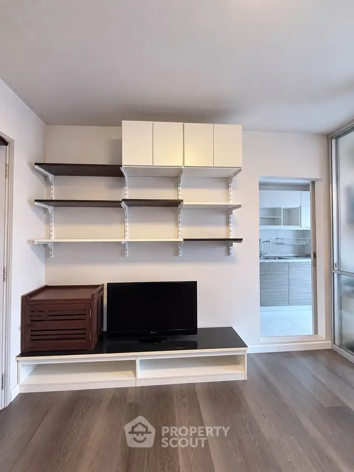Modern living room with sleek shelving and TV unit, showcasing minimalist design and open kitchen view.