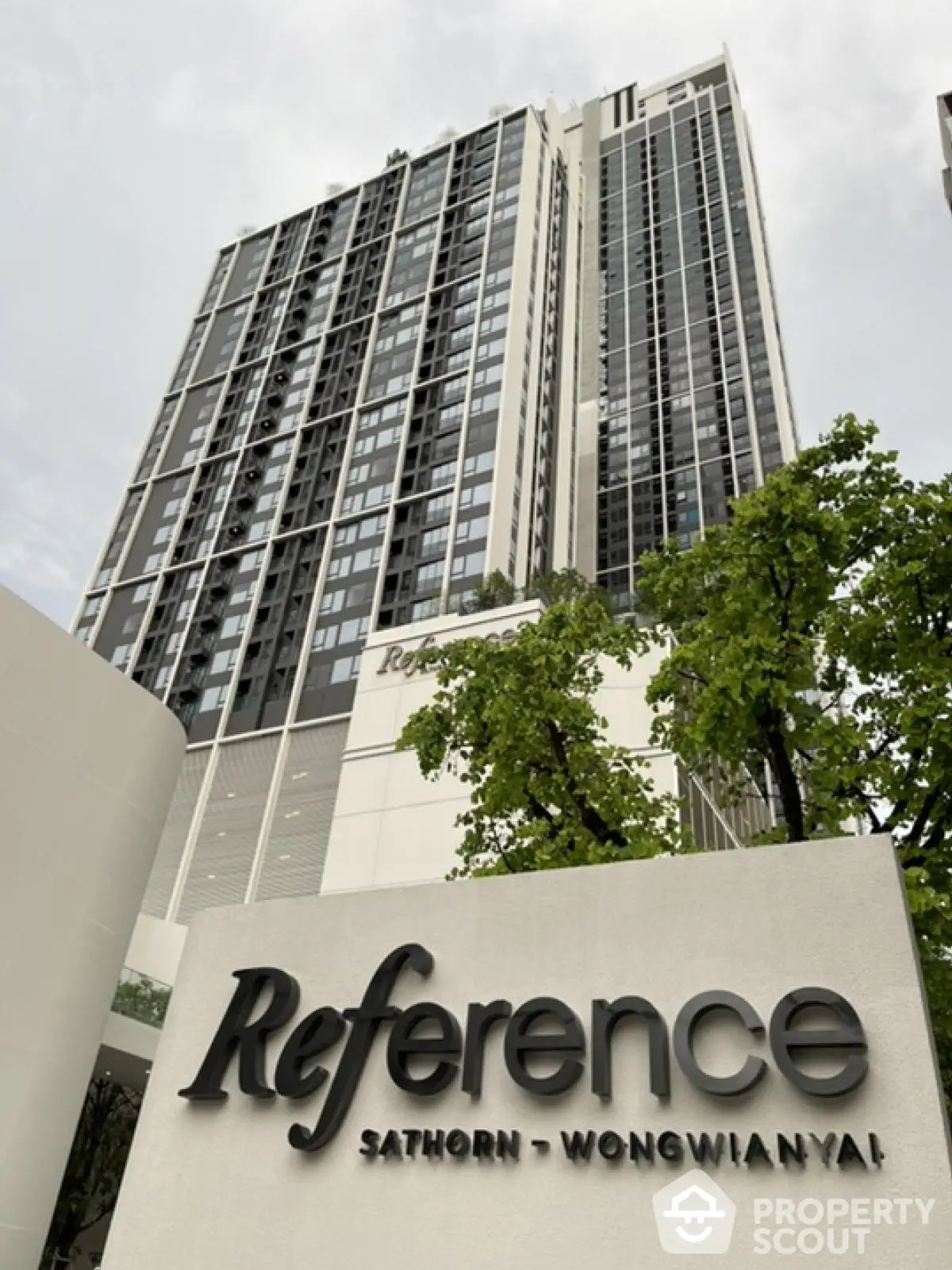 Modern high-rise building with sleek design in Sathorn-Wongwianyai area, surrounded by lush greenery.