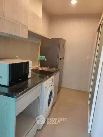 Modern kitchen with washing machine, microwave, and fridge in compact layout