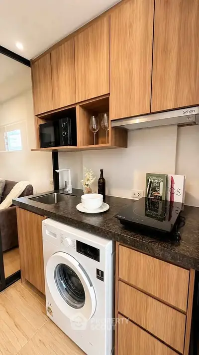 Modern kitchen with wooden cabinets, washing machine, and sleek appliances in a cozy apartment.