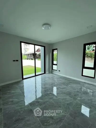 Spacious room with large windows and glossy tiled floor, overlooking a lush garden.