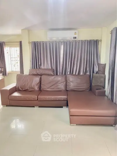 Spacious living room with modern brown leather sofa and elegant curtains, perfect for relaxation.