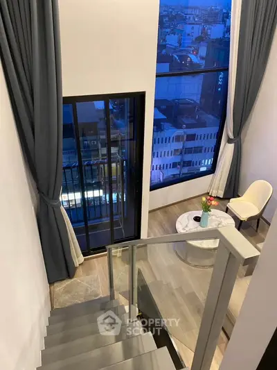 Elegant duplex interior with floor-to-ceiling windows and city view, featuring modern staircase and cozy seating area.
