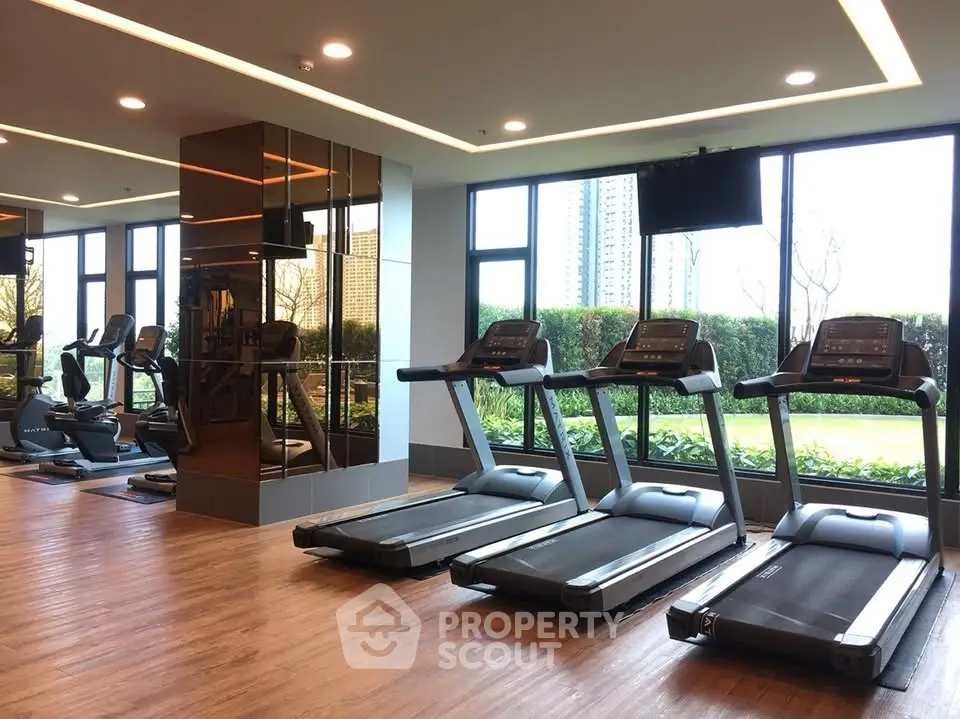 Modern gym with treadmills and large windows offering garden views in luxury apartment complex.