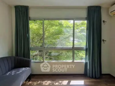 Bright living room with large window and green view, featuring elegant curtains and a cozy sofa.