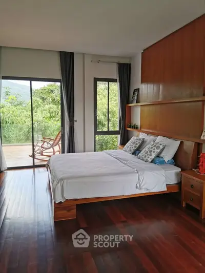 Spacious bedroom with wooden flooring and large windows opening to a scenic balcony view.