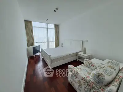 Spacious bedroom with wooden flooring and large window offering natural light.