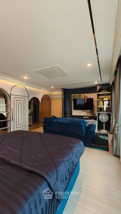 Luxurious bedroom with elegant decor, featuring a plush blue bed, stylish sofa, and modern entertainment setup.