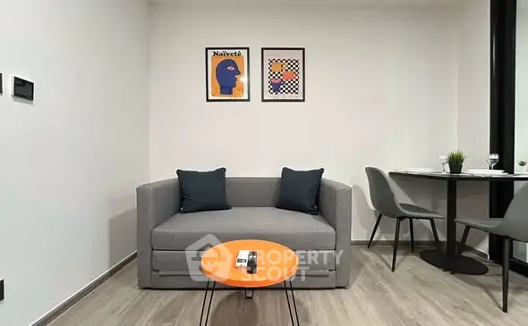 Modern living room with stylish gray sofa, vibrant orange table, and contemporary wall art.