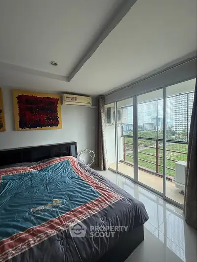 Spacious bedroom with balcony and city view, featuring modern decor and ample natural light.