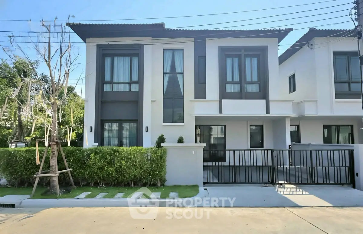 Modern two-story house with sleek design and gated entrance in a suburban neighborhood.