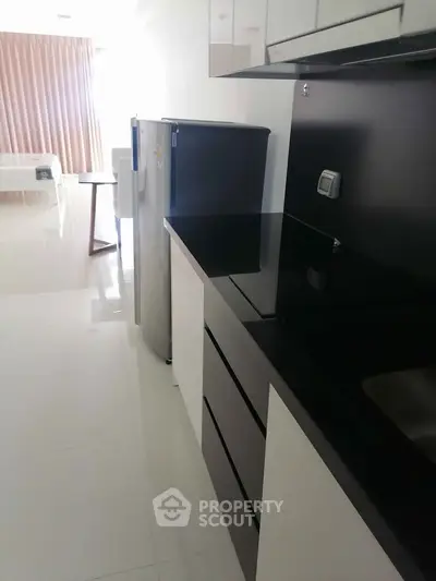 Modern kitchen with sleek black countertops and compact fridge in a bright apartment.