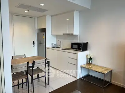 Modern kitchen with dining area, featuring sleek white cabinets and compact appliances.