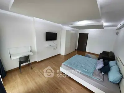 Spacious modern bedroom with wooden flooring and wall-mounted TV